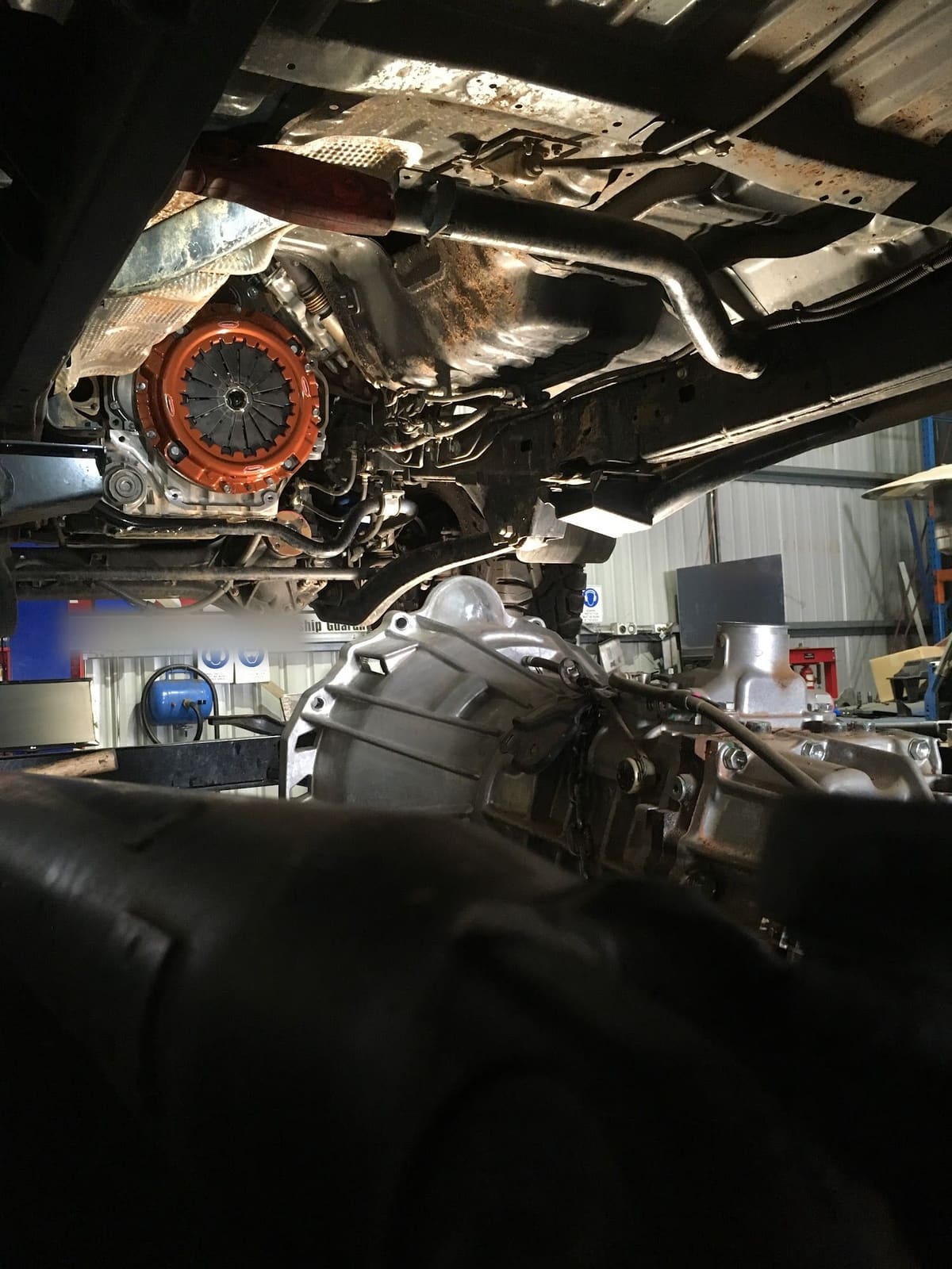 Looking up at the underside of a vehicle in the workshop with the clutch and gearbox exposed
