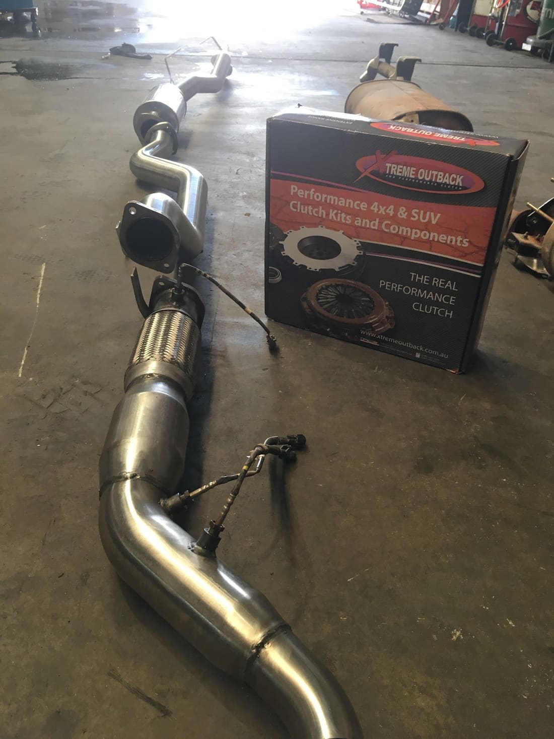An exhaust section and a boxed clutch kit on the workshop floor
